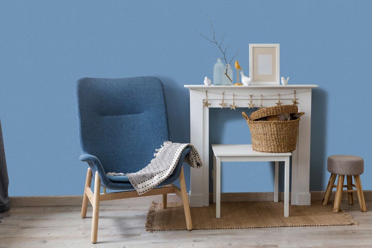 Blaue strukturierte Tapete in einem Wohnzimmer mit blauem Sessel, weißem Deko-Kamin, Weidenkorb und Jute-Teppich auf Holzfußboden.
