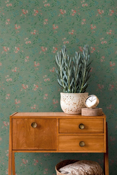 Szene mit einer weißen Skulptur, einer Zimmerpflanze und einer Tasse auf einem dunklen Tisch vor einer floralen Tapete.