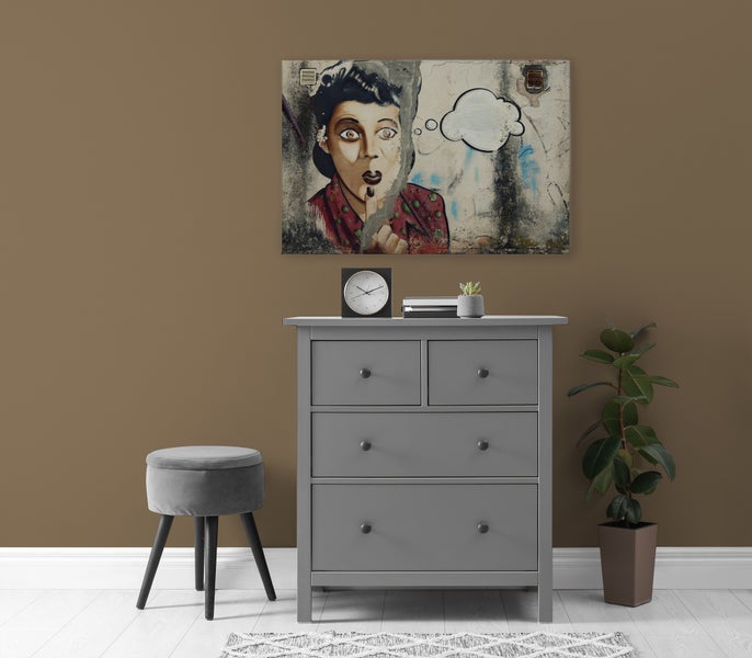 Eine Kommode mit vier Schubladen steht vor einer Wand mit einem Pop Art Wandbild, daneben ein Hocker und eine Zimmerpflanze.
