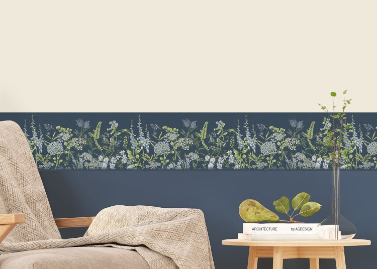 Tapetenbordüre mit floralem Muster aus Wildblumen auf einer dunkelblauen Wand in einem Wohnzimmer mit Sessel und Beistelltisch.