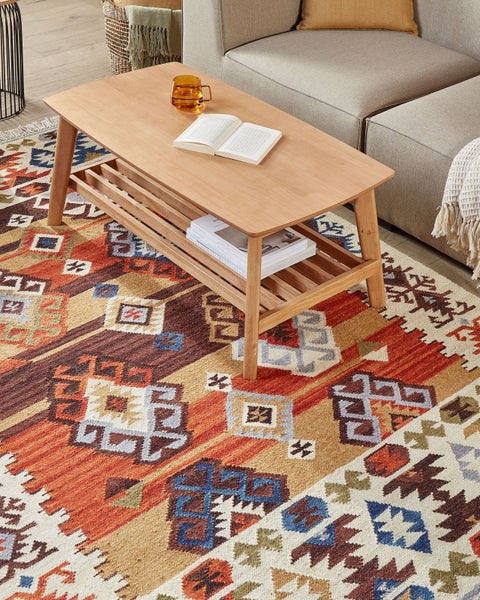 Wohnzimmer-Szene mit einem Couchtisch aus Holz auf einem gemusterten Teppich.