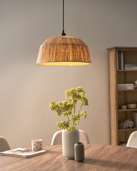 Hängeleuchte mit kuppelförmigem Schirm aus Rattan über einem Esstisch aus Holz in einem hellen Wohnraum.