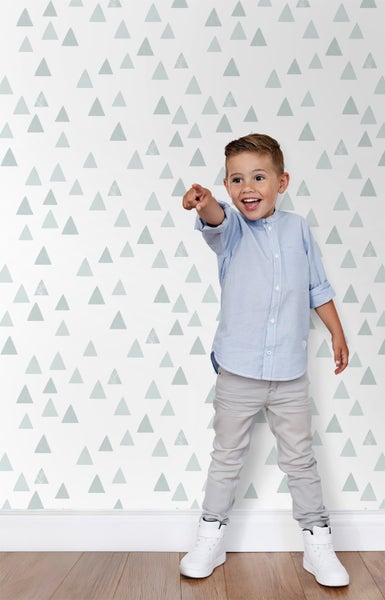 Ein Junge steht vor einer Wand mit Dreiecksmuster und deutet mit dem Finger.