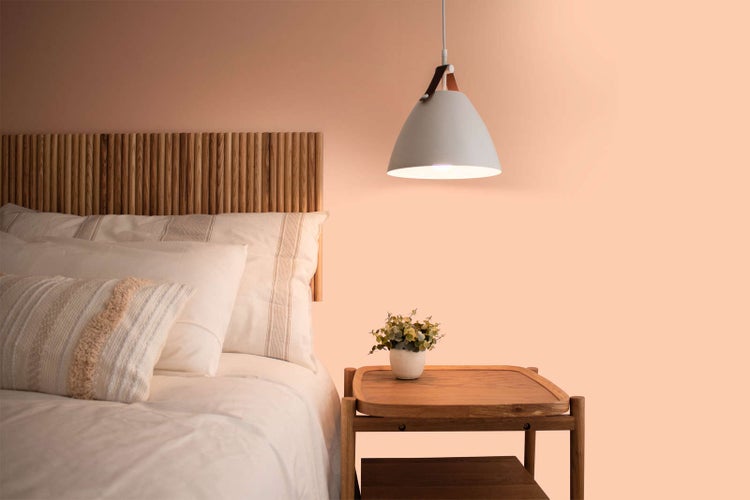 Modern und hell eingerichtetes Schlafzimmer mit Kopfteil aus Holzlamellen, hellem Bettzeug, passendem Nachttisch und einer Hängelampe.