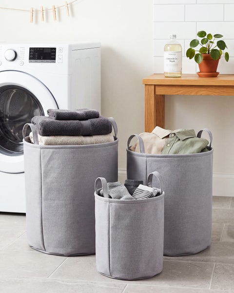 Drei runde Textil-Wäschekörbe in verschiedenen Größen vor einer Waschmaschine, gefüllt mit Handtüchern und Kleidung in einer hellen Waschküche.