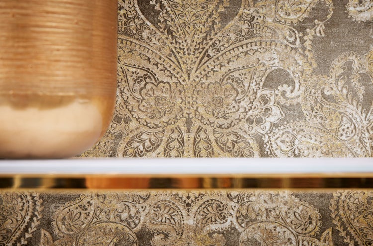 Innenraumszene mit einer Frau auf einem grünen Sessel vor einer gemusterten Tapete