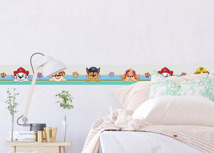 Selbstklebende Wandbordüre mit Paw Patrol Figuren in einem hellen Kinderzimmer mit Bett und Nachttischlampe.