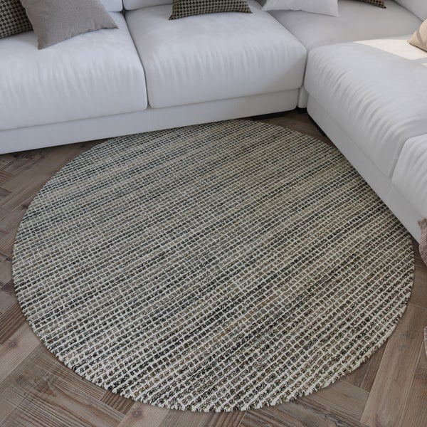 Runder, gewebter Teppich mit Strukturmuster im hellen Wohnzimmer vor einem Sofa auf Holzparkett.