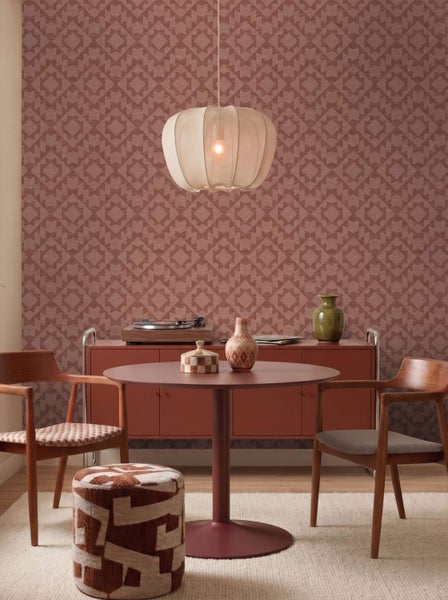 Ein modern eingerichtetes Esszimmer mit gemusterter Tapete, einem runden Tisch, Holzstühlen, einem Pouf und einer runden Pendelleuchte.