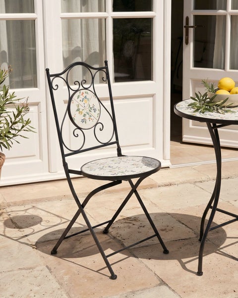 Klappbarer Gartenstuhl aus Metall mit Mosaik-Sitzfläche und Rückenlehne mit floralem Muster auf einer Terrasse.