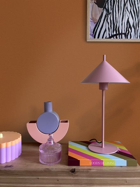 Moderne Tischleuchte mit kegelförmigem Schirm, Dekovasen aus Keramik und eine Glasdose auf einem Holzregal vor einer Wand.