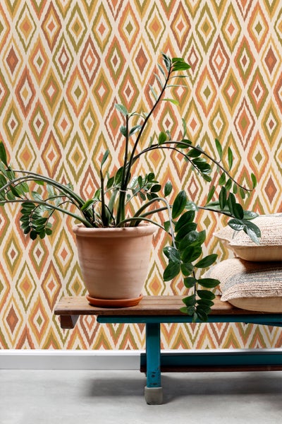 Szene mit gemusterter Tapete, Zimmerpflanze im Topf und Kissen auf einer Bank