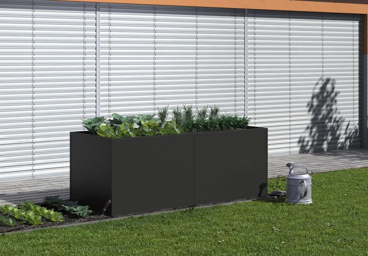 Dunkles Hochbeet aus Metall, bepflanzt mit Kräutern und Gemüse, auf einer Rasenfläche neben einer Gießkanne und einer Terrasse.