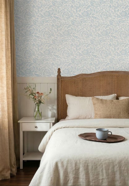 Helle Vliestapete mit blauem Blumenmuster in einem Schlafzimmer im Landhausstil mit Holzbett und weißem Nachttisch.