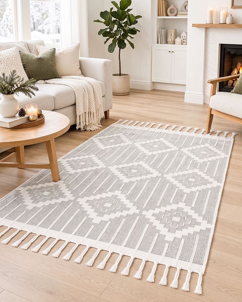 Wohnzimmer mit hellem Sofa, Couchtisch und einem rechteckigen Webteppich mit geometrischem Rautenmuster und Fransen an den kurzen Seiten.
