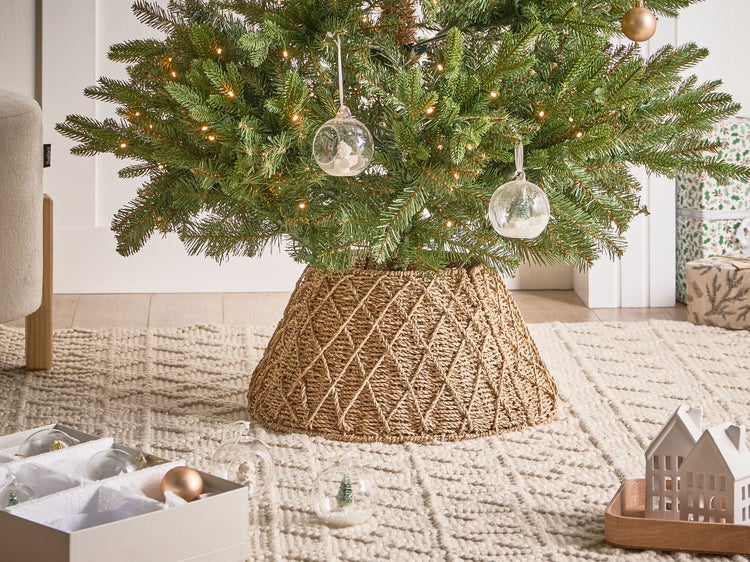 Weihnachtsbaum mit Lichterkette, Baumschmuck und Weidenkorb als Baumständer auf einem Teppich