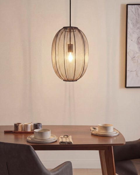 Moderne Pendelleuchte mit ovalem Drahtgeflechtschirm über einem Holzesstisch mit Geschirr in einem hellen Raum.