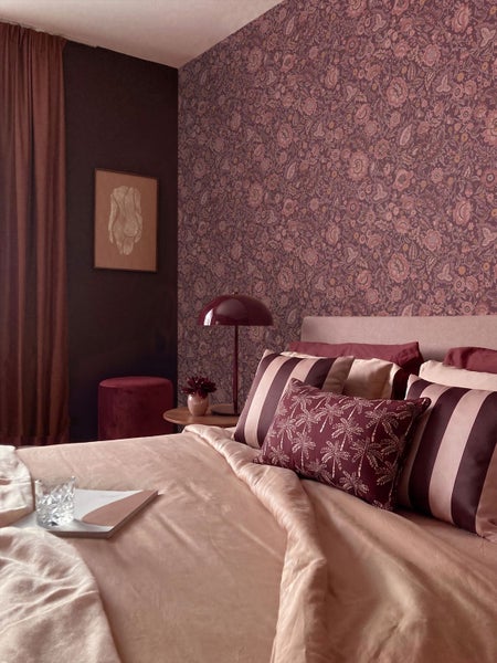 Vliestapete mit floralem Muster aus Rosen und Blättern an einer Wand hinter einem Holztisch mit runden Keramikvasen.
