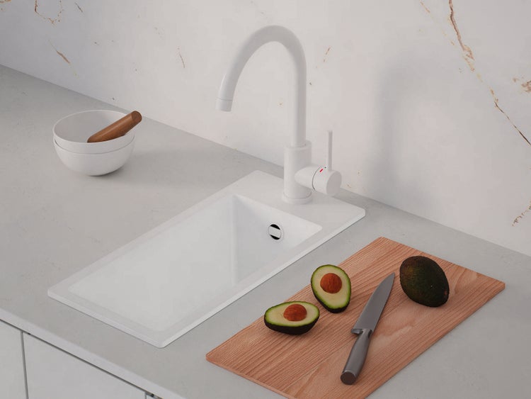 Weiße Küchenspüle mit weißer Mischbatterie in moderner Küche mit grauer Arbeitsplatte und Zubehör wie Schneidebrett und Mörser.