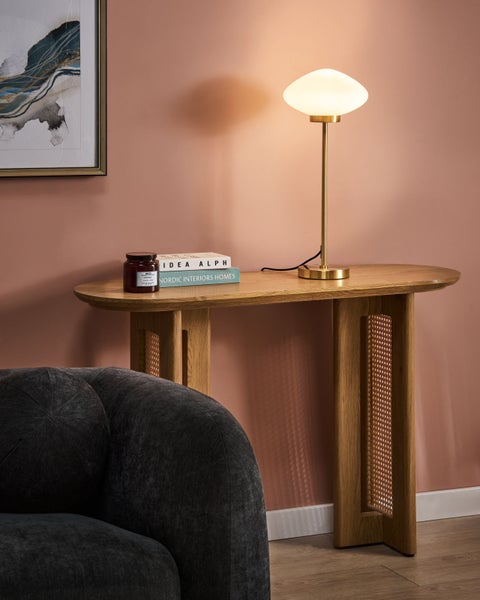 Dekorative Szene mit einem Holztisch, einer Lampe, einem Buch, einer Duftkerze und einem Teil eines Sessels.