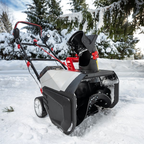 Eine Schneefräse steht auf einer verschneiten Fläche vor Nadelbäumen zur Schneeräumung bereit.