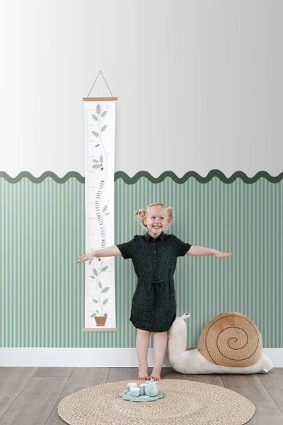 Mädchen mit Wachstumsmesslatte mit Eichenmotiv im Kinderzimmer