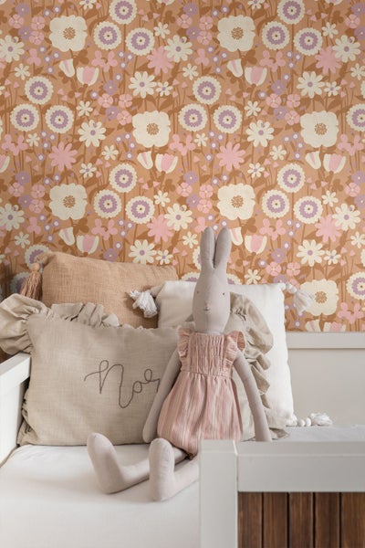 Vliestapete mit Blumenmuster im Retro-Stil in einem Kinderzimmer hinter einem Bett mit Kissen und Spielzeughasen.