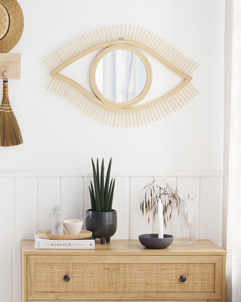 Dekoratives Interieur mit Spiegel in Augenform, Kommode, Zimmerpflanze und Accessoires.