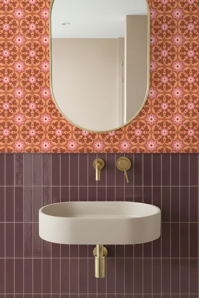 Modernes Badezimmer mit beigem ovalem Waschbecken, goldener Wandarmatur, dunkelvioletten vertikalen Fliesen, gemusterter Tapete und ovalem Spiegel.