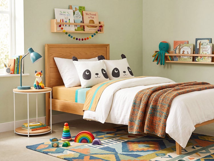 Ein Kinderzimmer mit einem Holzbett, Panda-Kissen, Bücherregalen, Nachttisch, Spielzeug und einem gemusterten Teppich in einer fröhlichen Umgebung.