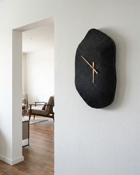 Wanduhr mit unregelmäßiger Form und goldenen Zeigern in einem Wohnraum.