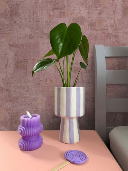 Dekorative Szene mit Zimmerpflanze im gestreiften Topf, Kerze und Wachsfigur auf einem Tisch