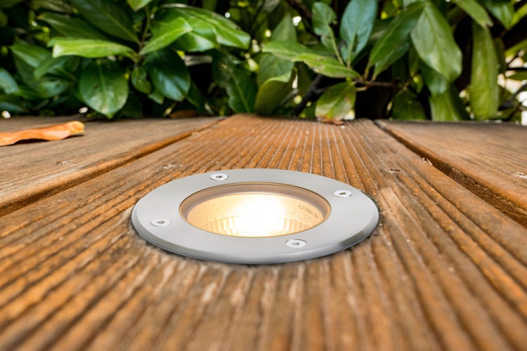 Bodeneinbaustrahler auf einer Holzterrasse mit grünen Pflanzen im Hintergrund