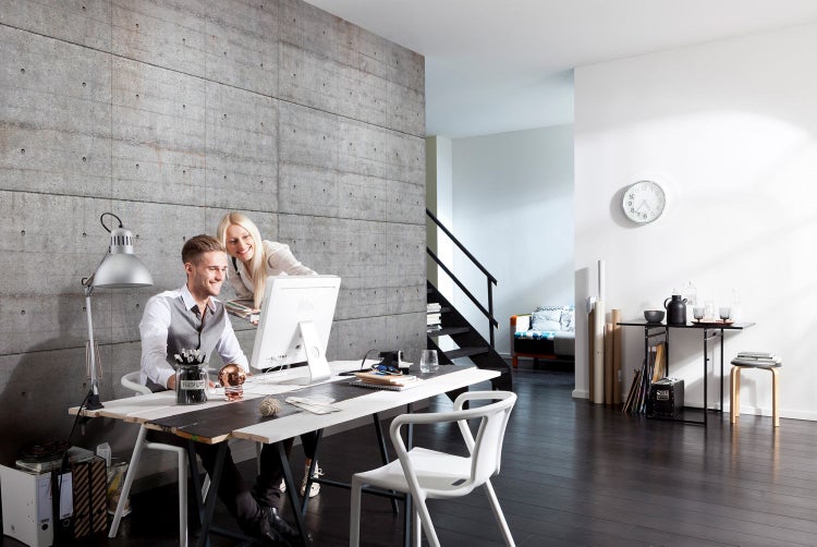 Büro mit Betonwand, Schreibtisch, Stühlen und zwei Personen