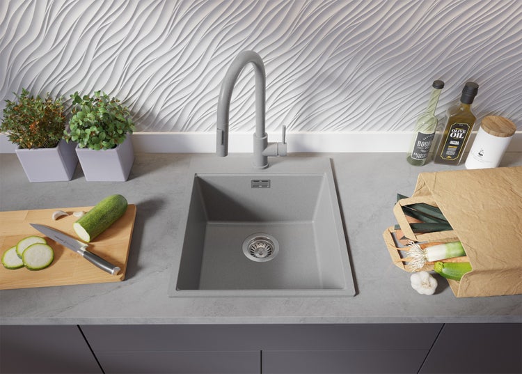 Spüle aus Stein mit Wasserhahn, Kräutern, Schneidebrett und Lebensmitteln in einer Einkaufstasche