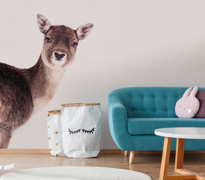 Fototapete mit einem realistischen Reh im Kinderzimmer neben einem blauen Sofa, Aufbewahrungssäcken und einem runden Beistelltisch.