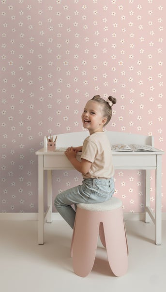 Ein Mädchen sitzt an einem weißen Schreibtisch vor einer rosafarbenen Tapete mit Blumenmuster.
