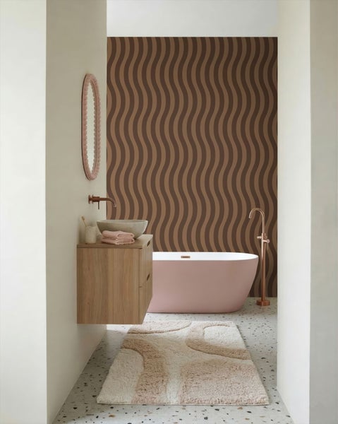 Modernes Badezimmer mit freistehender Badewanne, Holzwaschtisch mit Steinwaschbecken und gewellter Tapete. Kupferarmaturen und runder Spiegel.