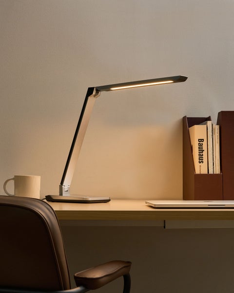 LED-Tischleuchte auf einem Schreibtisch mit Buch, Zeitschrift und Tasse