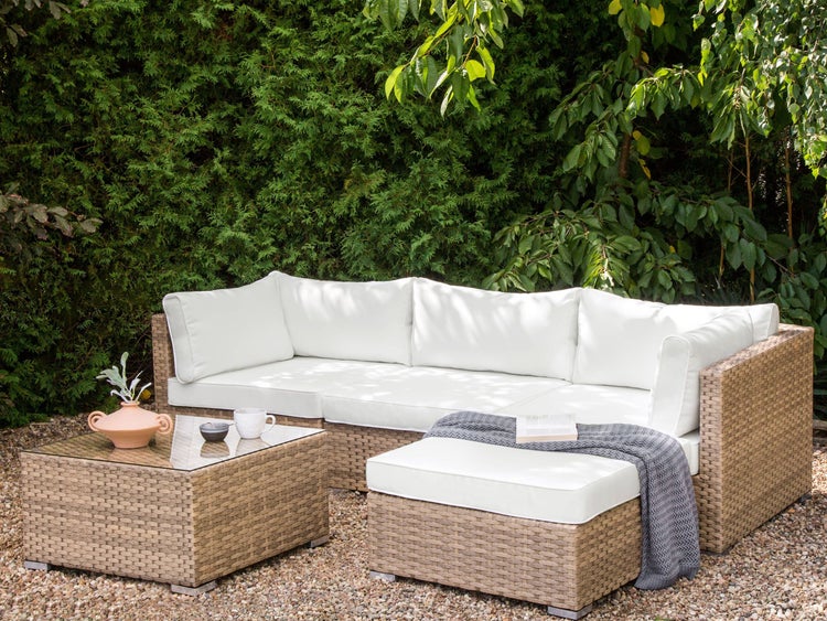 Gartenszene mit Rattansofa, Tisch und Hocker mit weißen Auflagen