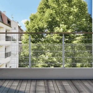 Modernes Balkongeländer mit Holzhandlauf und Edelstahlseilen auf einer hellen Terrasse mit Holzdielen vor grünen Bäumen.