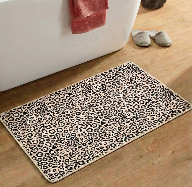 Rechteckige Badematte mit Leopardenmuster auf einem Holzboden neben einer Badewanne in einem hellen Badezimmer.