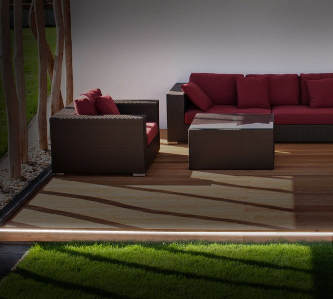 Gartenlounge-Set mit Sofa, Sessel und Tisch auf einer Holzterrasse mit Rasenfläche und Beleuchtung