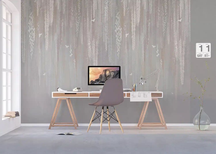 Hell eingerichtetes Arbeitszimmer mit einem Schreibtisch auf Holzböcken und einer Fototapete mit herabhängendem Blättermuster.
