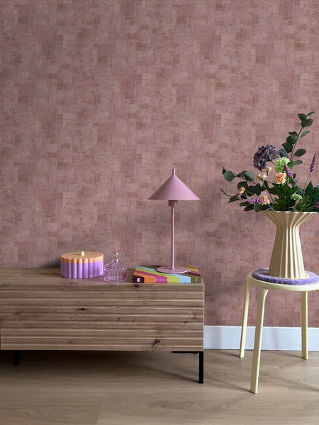 Innenraum mit einer Wand mit Mustertapete, einem Holzschrank, einer Tischlampe und einem Blumenarrangement.