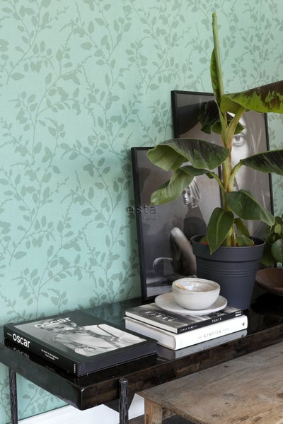 Dekorative Wand mit blattgemusterter Tapete, kombiniert mit Pflanzen und dekorativen Büchern