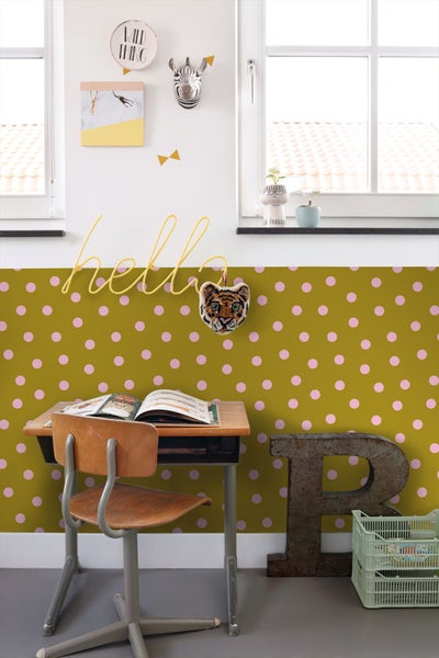 Vliestapete in Grün mit rosa Punkten in einem hellen Kinderzimmer mit Holztisch, Stuhl und Wanddekoration.