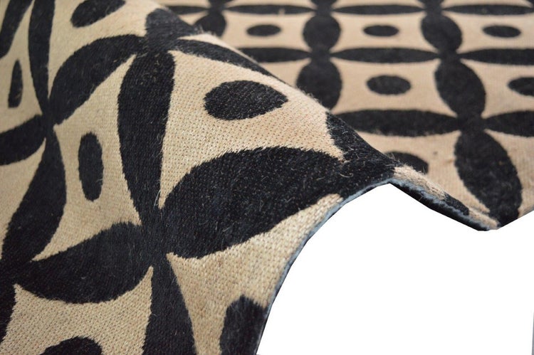 Detailaufnahme eines gewebten Teppichs mit schwarzem geometrischem Muster auf beigem Hintergrund.