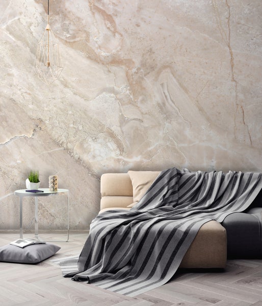 Helles Wohnzimmer mit einer Fototapete in Marmoroptik, einem beigen Sofa mit gestreifter Decke, einem Beistelltisch und einer Draht-Pendelleuchte.
