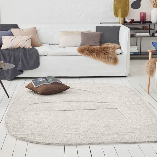 Heller Teppich mit abgerundeten Ecken und Linienstruktur in einem hellen Wohnzimmer mit Sofa, Kissen und Holzdielen.